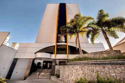 a building with palm trees in front of it at Slim Curitiba Alto da XV in Curitiba