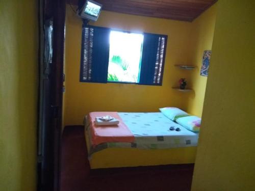 a small yellow room with a bed and a window at Pousada E Restaurante Passart in Morro de São Paulo