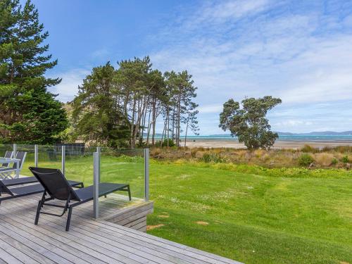 a deck with a chair and a bench on the grass at Beachfront Escape - Snells Beach Holiday Home in Snells Beach