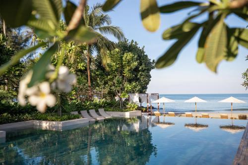 a swimming pool next to the ocean with umbrellas at VAYNA Boutique Koh Chang in Ko Chang