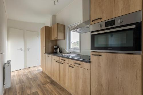 a kitchen with wooden cabinets and a sink and a microwave at Welcome in - Vakantiepark Fort den Haak I Nabij strand en Veerse meer in Vrouwenpolder