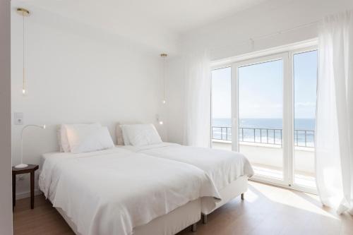 a white bedroom with a bed and a large window at Blue Buddha Beach Rooms & Suites in Ericeira