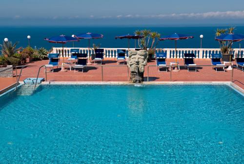 a swimming pool with chairs and umbrellas and the ocean at Hotel Grazia alla Scannella in Ischia