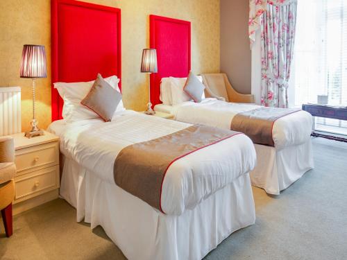 2 Betten in einem Hotelzimmer mit roten Fenstern in der Unterkunft OYO Lamphey Hall Hotel in Pembroke