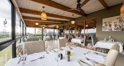 um restaurante com mesas e cadeiras brancas e janelas em De Zeekoe Guest Farm em Oudtshoorn