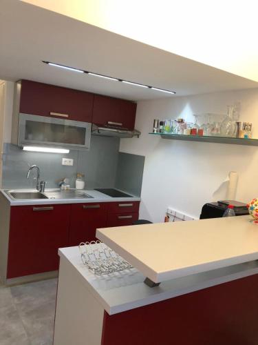 La cuisine est équipée de placards rouges, d'un évier et d'un comptoir. dans l'établissement Naturiste Cap d'Agde Villa Héliovillage 116, au Cap d'Agde