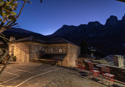 a stone building with two red chairs on a patio at Papaevangelou Hotel in Papigko