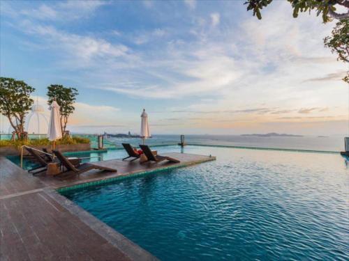 einen Pool mit Stühlen und das Meer im Hintergrund in der Unterkunft Wongamat Tower High Floor&Seaview in Pattaya North