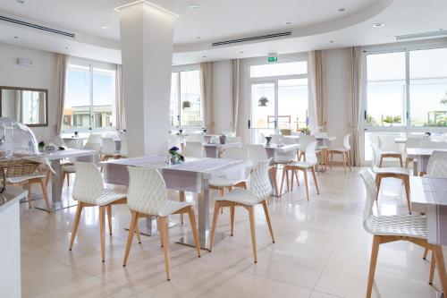 un restaurant avec des tables blanches, des chaises et des fenêtres dans l'établissement Hotel Riviera, à Bellaria-Igea Marina