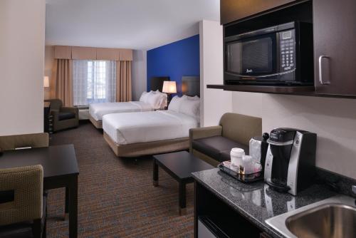 ベーカーズフィールドにあるHoliday Inn Express & Suites Bakersfield Airport, an IHG Hotelのベッドとリビングルームが備わるホテルルームです。