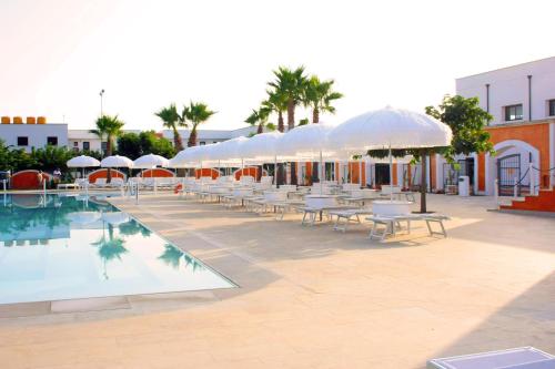 a pool with white umbrellas and tables and chairs at Chiusurelle Village Resort in Punta Prosciutto
