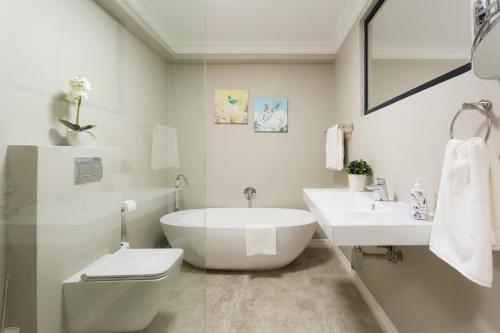 a white bathroom with a tub and a toilet and a sink at The Gregory in Pinetown