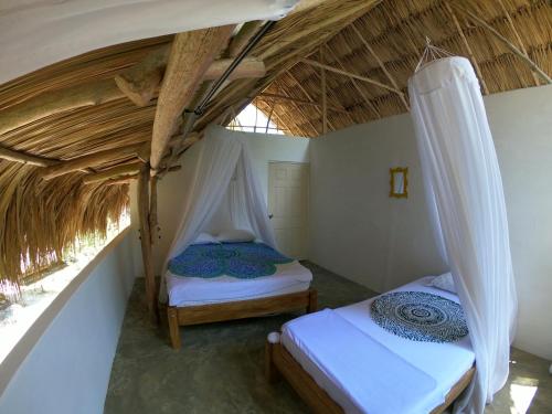 two beds in a room with a thatched roof at Hotel Jasayma dentro del Parque Tayrona in El Zaino