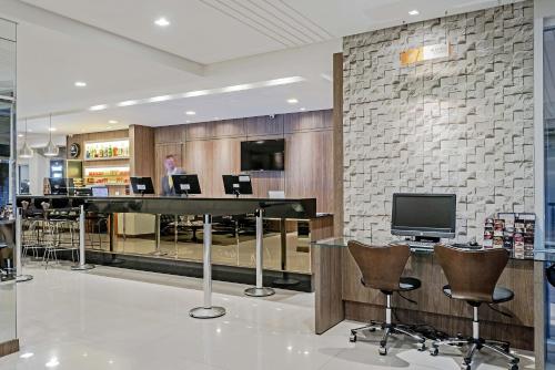 a lobby with a bar with chairs and a television at Slim Curitiba Av das Torres in Curitiba