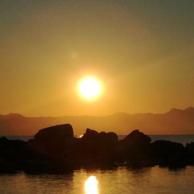 a sunset with the sun setting over the water at Apartments Zoumperi in Nea Makri