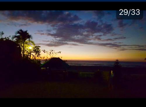 a sunset at the beach with a tent and a palm tree at Seabreeze Beachfront Home and Cottages new management in San Juan