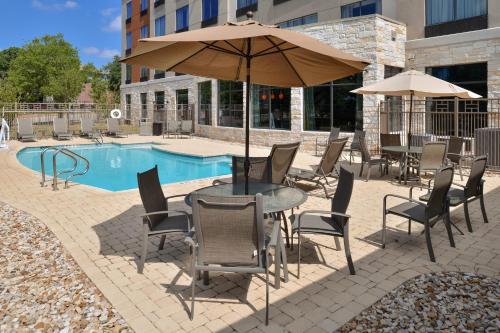 a table and chairs with an umbrella next to a pool at Holiday Inn Express & Suites Austin South by IHG in Austin