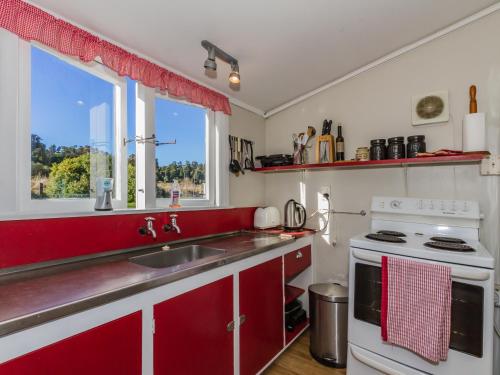 eine Küche mit roten Schränken, einem Waschbecken und einem Fenster in der Unterkunft Ohakune Cottage - Ohakune Holiday Home in Ohakune