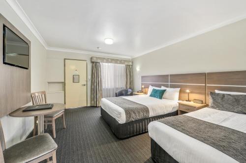a hotel room with two beds and a desk at Quality Inn Ashby House Tamworth in Tamworth