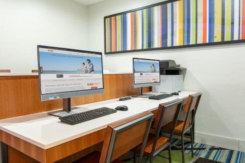 two computer monitors sitting on a desk with chairs at Holiday Inn Express Hotel & Suites Seaside Convention Center by IHG in Seaside