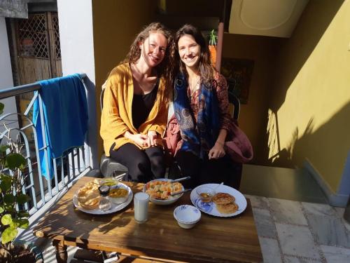 two women sitting on a balcony with food on a table at Gungun Homestay in Rishīkesh