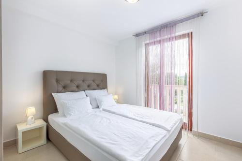 a white bedroom with a large bed with a window at Apartments Mike in Malinska