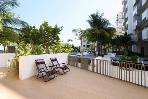 two chairs on a balcony with a fence and palm trees at By The Sea Beach Front Apartment in Batu Ferringhi