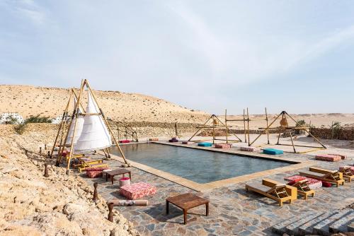 einen Pool in der Wüste mit Stühlen und einem Segelboot in der Unterkunft Les Dunes de Dakhla in Ad-Dakhla