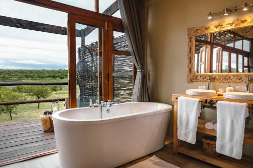 Cheetah Ridge Lodge في نامبيتي جيم ريسيرف: حمام مع حوض استحمام و نافذة كبيرة
