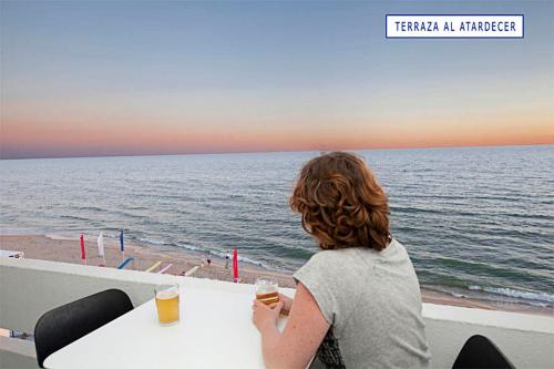 a woman sitting at a table looking at the ocean at Apartamento con vistas al mar primera linea playa Matalascañas in Matalascañas