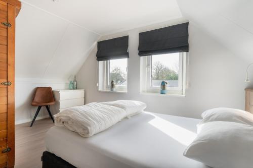 a bedroom with a white bed with two windows at Vakantiewoning Seaside in Oostkapelle