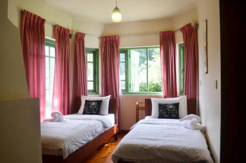 a bedroom with two beds and windows with red curtains at Samri Holiday Bunglow in Nuwara Eliya