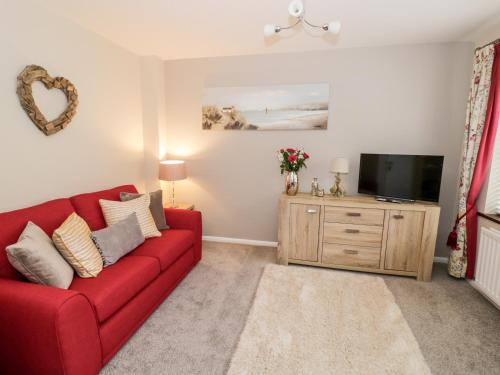 a living room with a red couch and a tv at Valentines Cottage in Stratford-upon-Avon