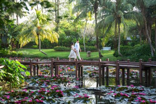 a couple walking across a bridge over a pond with flowers at JW Marriott Phuket Resort and Spa in Mai Khao Beach
