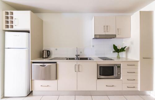 a kitchen with white cabinets and a sink and a refrigerator at Silkari Lagoons Port Douglas in Port Douglas