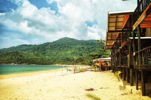 a beach with a building and the ocean and a mountain at Beachfront Hut Downstairs Astra - Beach Shack Chalet in Tioman Island