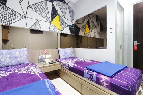 2 bedden in een kleine kamer met paarse lakens bij WISMA 9 Jakarta in Jakarta