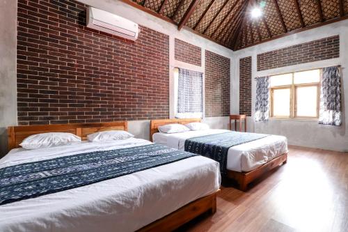 two beds in a room with a brick wall at Saka Homestay Boutique & Cafe in Borobudur
