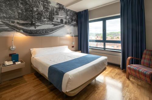 a bedroom with a bed, chair and a window at Aparthotel Campus in Oviedo