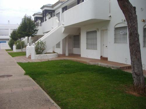 una casa blanca con un patio de hierba delante de ella en Playa de La Barrosa La Almadraba IV Fase "Interior" B-3, en Chiclana de la Frontera