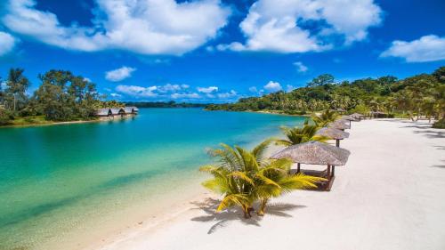 a beach with many straw umbrellas and the water at Holiday Inn Resort Vanuatu by IHG in Port Vila