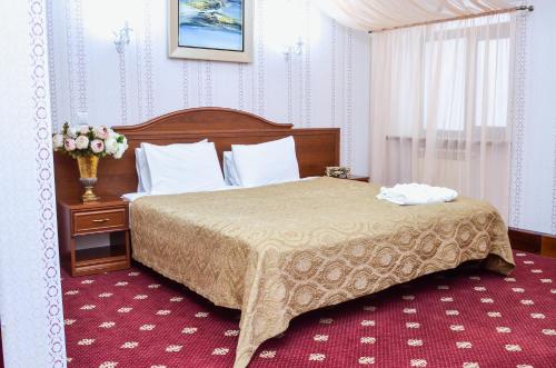 a bedroom with a bed and a vase of flowers on a table at Amsterdam Hotel Aktobe in Aktobe