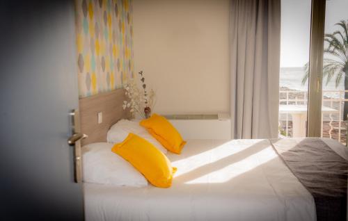 a bedroom with a bed with yellow pillows and a window at Hotel et Appartements Reine D'Azur in Roquebrune-Cap-Martin