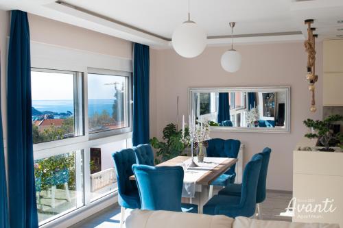 una sala da pranzo con sedie blu, tavolo e finestre di Apartmani Avanti Becici a Bečići