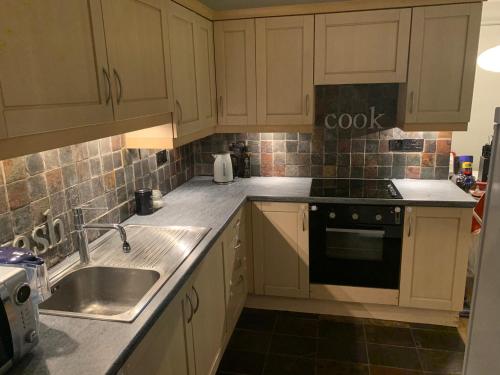 cocina con armarios blancos, fregadero y fogones en Stansted spacious 2-bed apartment, easy access to Stansted Airport & London, en Stansted Mountfitchet
