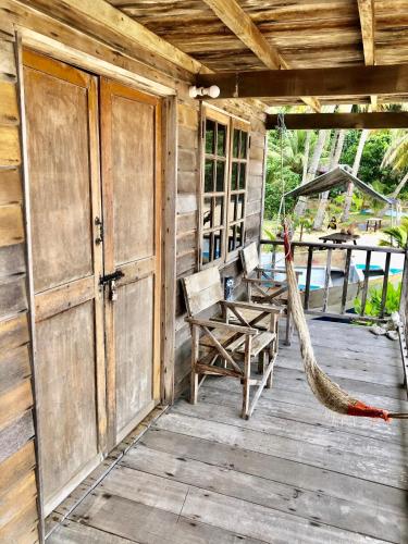 um alpendre em madeira com uma rede de descanso, uma mesa e cadeiras em Beachfront Hut Downstairs Astra - Beach Shack Chalet em Ilha Tioman