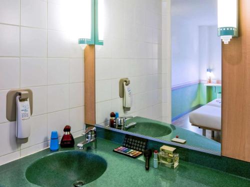 Ibis Budget Madrid Alcalá de Henares La Dehesa في ألكالا دي إيناريس: حمام مع حوض أخضر ومرآة