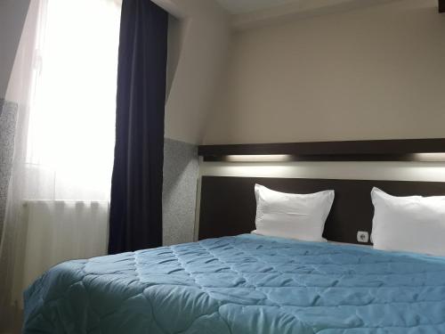 a bedroom with a blue bed with two pillows and a window at Prenoćište Konstantin 2008 in Niš
