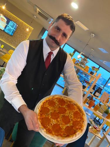 a man is holding a large pepperoni pizza at Hotel Moment in Velika Plana