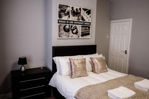 a bedroom with a bed with white sheets and gold pillows at Inspired Stays in Stoke on Trent